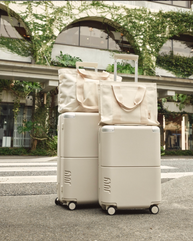 two cream colored rolling pieces of luggage with matching totes on top in front of a hotel